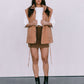 Woman wearing a tan vest over a white shirt and brown skirt with black boots on a plain background