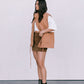 Woman wearing a tan vest, white shirt, brown skirt, and black boots against a white background