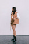 Woman wearing a tan vest, white shirt, brown skirt, and black boots against a white background