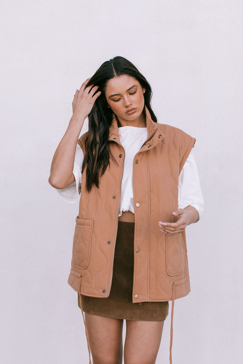 Woman wearing a brown vest over a white shirt and brown skirt on a white background