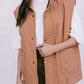 Person wearing a brown vest over a white shirt and black skirt on a plain background