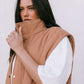 Woman wearing a brown puffer vest with white sleeves against a plain background