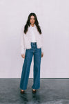 Woman wearing a white fluffy jacket and blue jeans against a white background