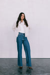 Woman wearing a white sweater and blue jeans against a plain background