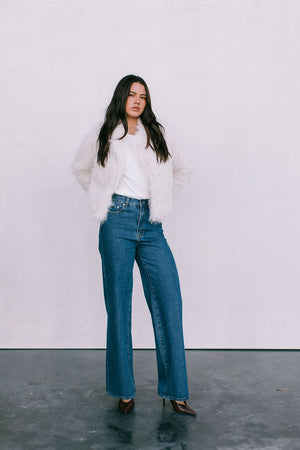 Woman wearing a white sweater and blue jeans against a plain background