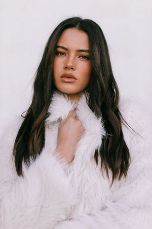 Woman wearing a white fur coat against a light background