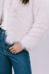 Person wearing a white fluffy jacket and blue jeans on a light gray background