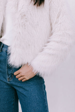 Person wearing a white fluffy jacket and blue jeans on a light gray background
